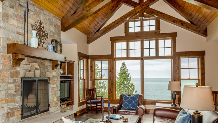 a large great room with windows overlooking a lake and custom beams